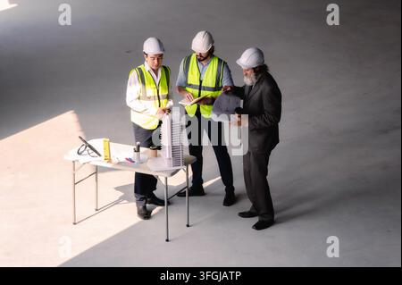 Real estate developers examining architectural model at empty space floor in building construction site, High angle view senior site managers with cor Stock Photo