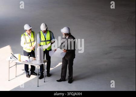 Real estate developers examining architectural model at empty space floor in building construction site, High angle view senior site managers and engi Stock Photo