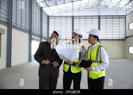 Engineers team and senior business review construction blueprint inside empty warehouse and reviewing architectural layout industrial building. Concep Stock Photo