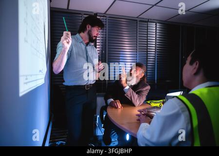 Engineering presenting and discuss floor plans on projector screen during late-night company meeting with senior project manager. Concept of brainstor Stock Photo