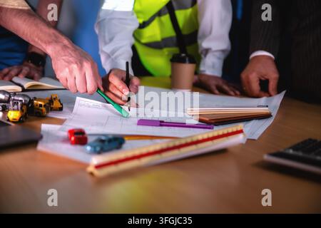 Construction management team discussing building layout paper on desk. Close-up hand while write shot. Concept of project planning, schedule of work, Stock Photo
