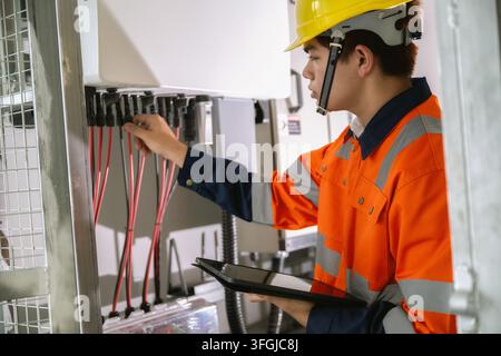 Young asian technician using tablet tracking solar power electrical circuit, checking industrial wiring setup with tablet, checking electric lines on Stock Photo