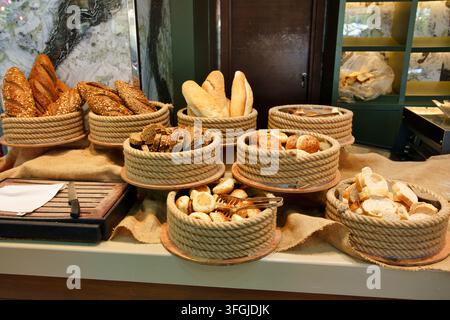 An assortment of freshly baked bread, baguettes, bread rolls, and sliced whole grain loaves displayed in decorative rope-wrapped baskets on burlap clo Stock Photo