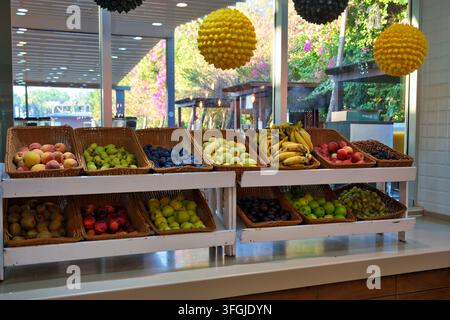 A wide variety of fresh ripe fruits arranged in woven wicker baskets on white wooden shelf units. Includes bananas, apples, pears, peaches, plums, kiw Stock Photo