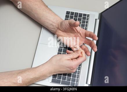 Male hand suffers from cramp, nerve pain, top down view. Illness while using laptop, office work Stock Photo
