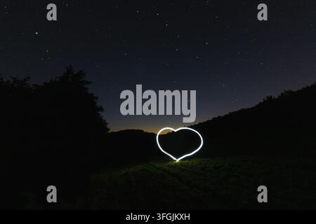 A glowing heart created with light painting technique in a meadow under a starry night sky Stock Photo