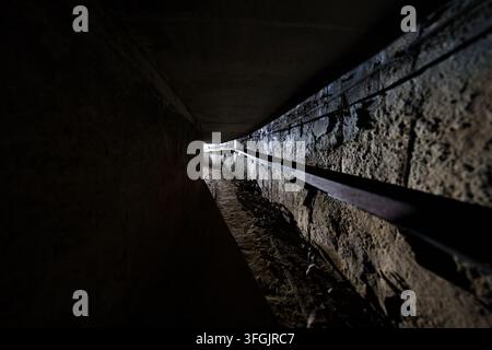 Dark narrow underground tunnel with light at the exit in abandoned Heilstätte Grabowsee, Germany. Urbex lost place decay. Stock Photo
