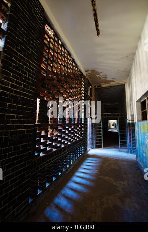Sunlight casts dramatic blue shadows through a perforated brick wall in a hallway of the abandoned Grabowsee sanatorium in Germany. Stock Photo