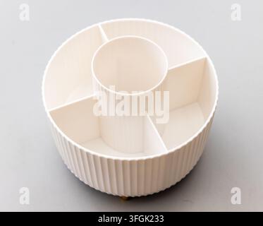 A creamcolored round plastic organizer with multiple compartments on a grey background Stock Photo