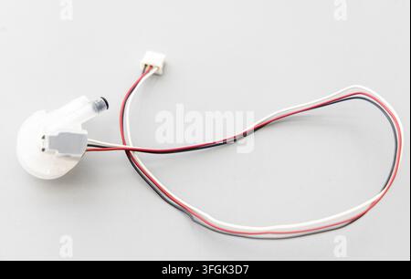 A white electronic component with colored wires sits on a grey surface Stock Photo