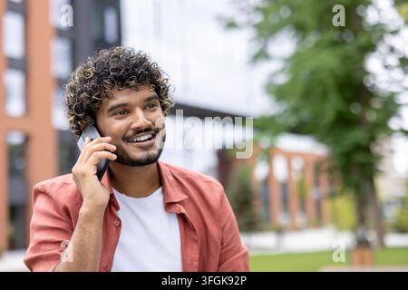 Cheerful student talking on mobile phone outdoors during university break smiling and looking away. Stock Photo