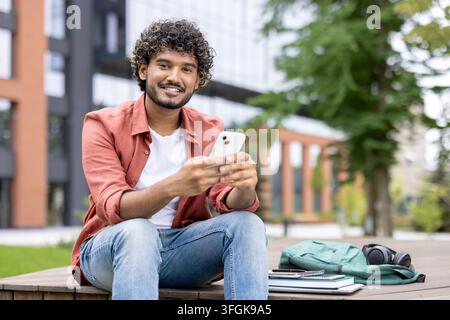 Smiling student drinking takeaway coffee and using smartphone during study break on campus grounds. Stock Photo