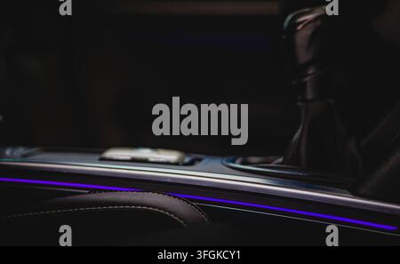 Modern car interior close-up of a center console featuring ambient purple lighting and a gear shifter in a dark luxury cabin. Stock Photo