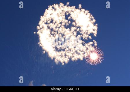 A unique daytime fireworks explosion creating a dense white smoke cloud and radial spark patterns in the blue sky. Stock Photo