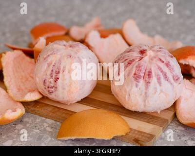Two peeled whole grapefruits on a wooden cutting board surrounded by pieces of citrus peel. Stock Photo
