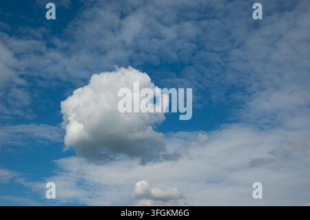 Blue sky with fluffy white clouds and a single distinctive cloud with an unusual shape. Stock Photo