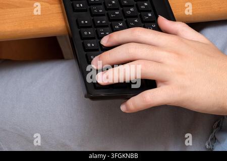 A close up shot of a caucasian person hand typing on a black computer keyboard at a wooden desk Stock Photo