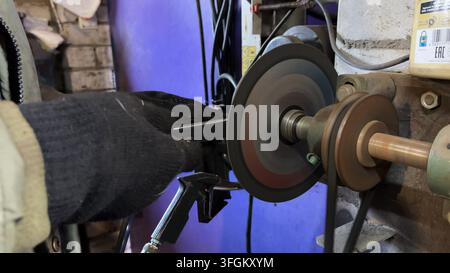 Arms of professional repairman grinding metal details with circular saw at garage. Male hands in protective gloves of mechanic polishing iron using Stock Photo