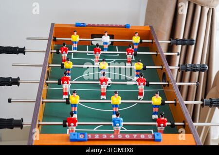 A closeup view of a tabletop foosball game showing miniature soccer players in red and yellow uniforms arranged on a green playing field. Stock Photo