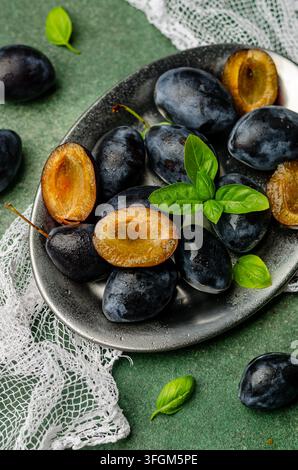 Fresh Ripe Plums with Green Basil Leaves on a Metal Plate Stock Photo