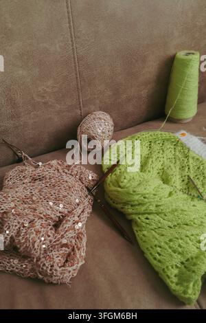 Bright neon green cardigan and beige sweater with gold sequins on wooden needles. Beautiful knitting pattern. Knitted fashion. Stock Photo