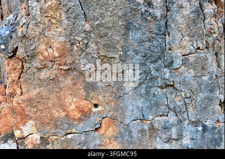 Close-up horizontal photograph of a rough stone wall surface showing weathered textures, cracks, and earthy mineral tones. Stock Photo