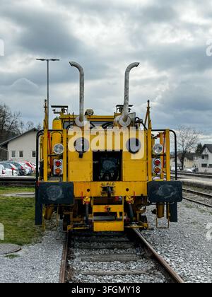 Front view of yellow Plasser and Theurer Unimat railway maintenance machine, heavy-duty industrial railroad equipment on tracks under dramatic sky Stock Photo