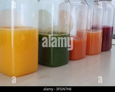 Five transparent glass bottles arranged in a row on a light-colored wooden surface, each containing different colored liquids. From left to right: Stock Photo