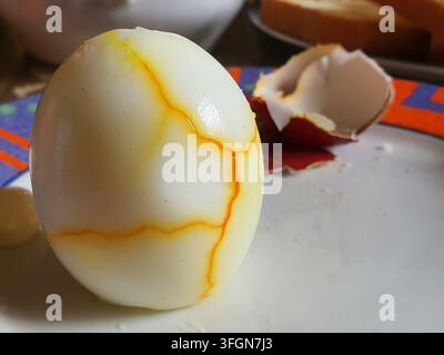 A close-up macro photograph of a peeled hard-boiled egg displaying distinctive orange-yellow marbling patterns on the white albumen surface. The Stock Photo
