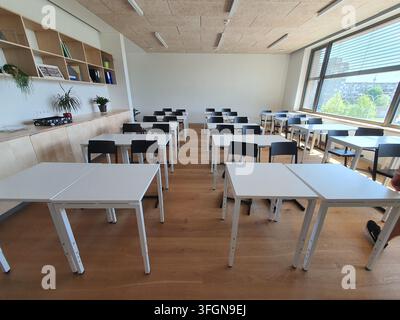 A bright, modern classroom or training room interior featuring rows of white desks and black chairs arranged on a light wooden floor. The room has Stock Photo
