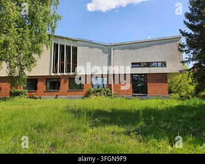 A modernist two-story building featuring a distinctive curved roofline and mixed material facade with red brick on the lower level and weathered Stock Photo
