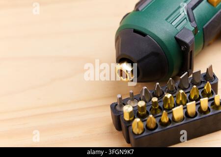 Modern green cordless electric screwdriver on wooden table. Black plastic holders filled with various golden and gray precision bits Stock Photo