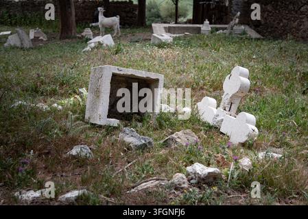 Deserted, abandoned broken Christian orthodox stone crosses and grave markers in a grassy rural cemetery with trees and a stone wall. Stock Photo
