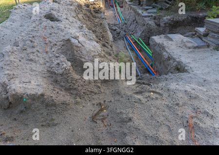 Cable laying in an open soil trench along a street during roadwork Stock Photo