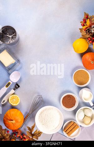 Assorted autumn baking ingredients  pumpkins, flour, eggs, butter, milk, sugar, spices, cocoa and lemons  with tools arranged in a light blue flat lay Stock Photo