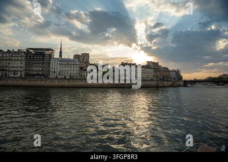 Panoramic view of the Seine River, Île de la Cité, and Notre-Dame spire framed by dramatic sunbeams bursting through clouds at sunset in Paris, France Stock Photo