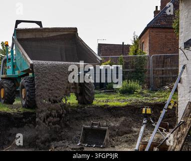 Compact site dumper unloading concrete into a freshly excavated trench beside residential buildings during backyard construction Stock Photo