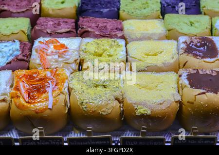 Rows of soft Asian bread buns topped with crab stick, garlic butter, sugar, and chocolate spreads on a retail display rack. Stock Photo