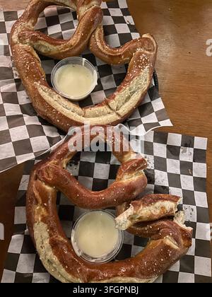 Two large soft pretzels with cheese sauce on a wooden table Stock Photo
