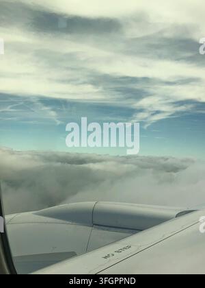 View of airplane wing, engine, and clouds from a plane window Stock Photo