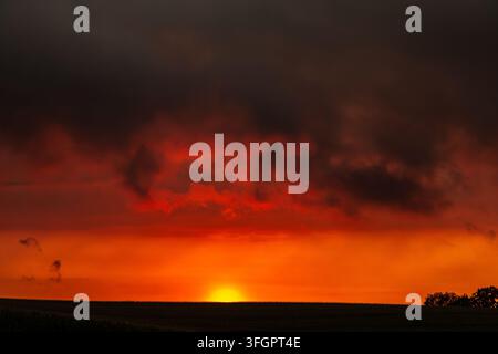 Dramatic orange sunset beneath dark storm clouds over a quiet rural horizon Stock Photo