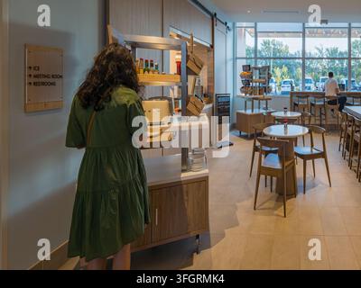 Arkansas, United States, SEP 05, 2026 - A woman in a green dress stands at a wooden self-service station with a toaster and condiments inside a Stock Photo