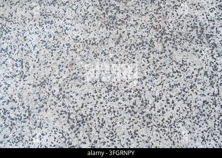 Close-up abstract texture of a speckled terrazzo surface with dense gray and dark aggregate particles embedded in a light concrete background. Stock Photo