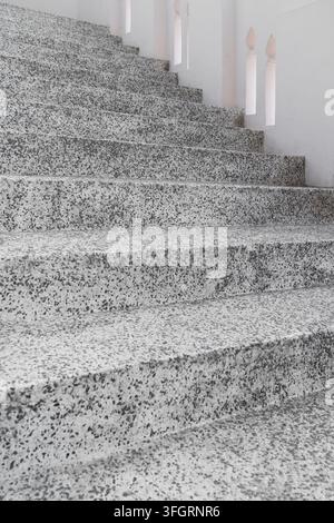 Close-up view of a speckled terrazzo staircase with textured gray steps and white decorative architectural balusters Stock Photo