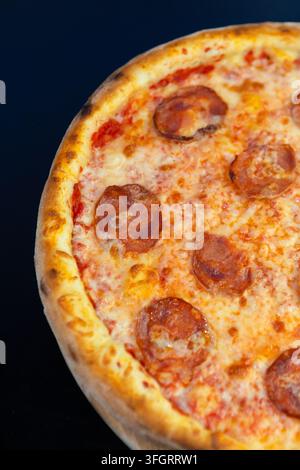 A large pepperoni pizza is placed on a wooden surface. The crust is golden brown and the cheese is melted. The pizza has several slices of pepperoni o Stock Photo