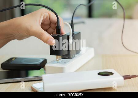 Person plugging or unplugging a black USB power charger adapter from an extension power socket strip on a table. Stock Photo