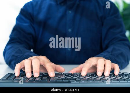 Person in dark blue shirt types on keyboard. Fingers poised over keys, focused and engaged. Suitable for business, work, or online activity themes. Ne Stock Photo