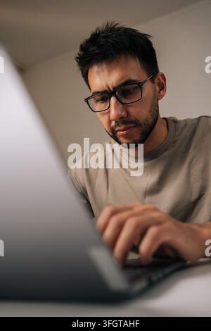 Bearded male freelancer focusing intently on laptop computer while working from remote home office setup, embodying modern work-from-home lifestyle wi Stock Photo