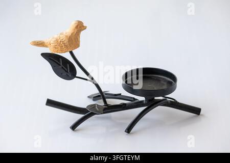 Side view of a rustic black metal tea light holder featuring a small wooden bird figurine perched on a leafy branch over white backdrop. Stock Photo