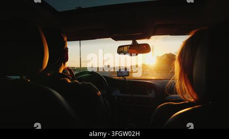 A young multi-ethnic couple is driving to the car in a sunset. The light beautifully illuminates the woman's hair. Dream to travel concept Stock Photo